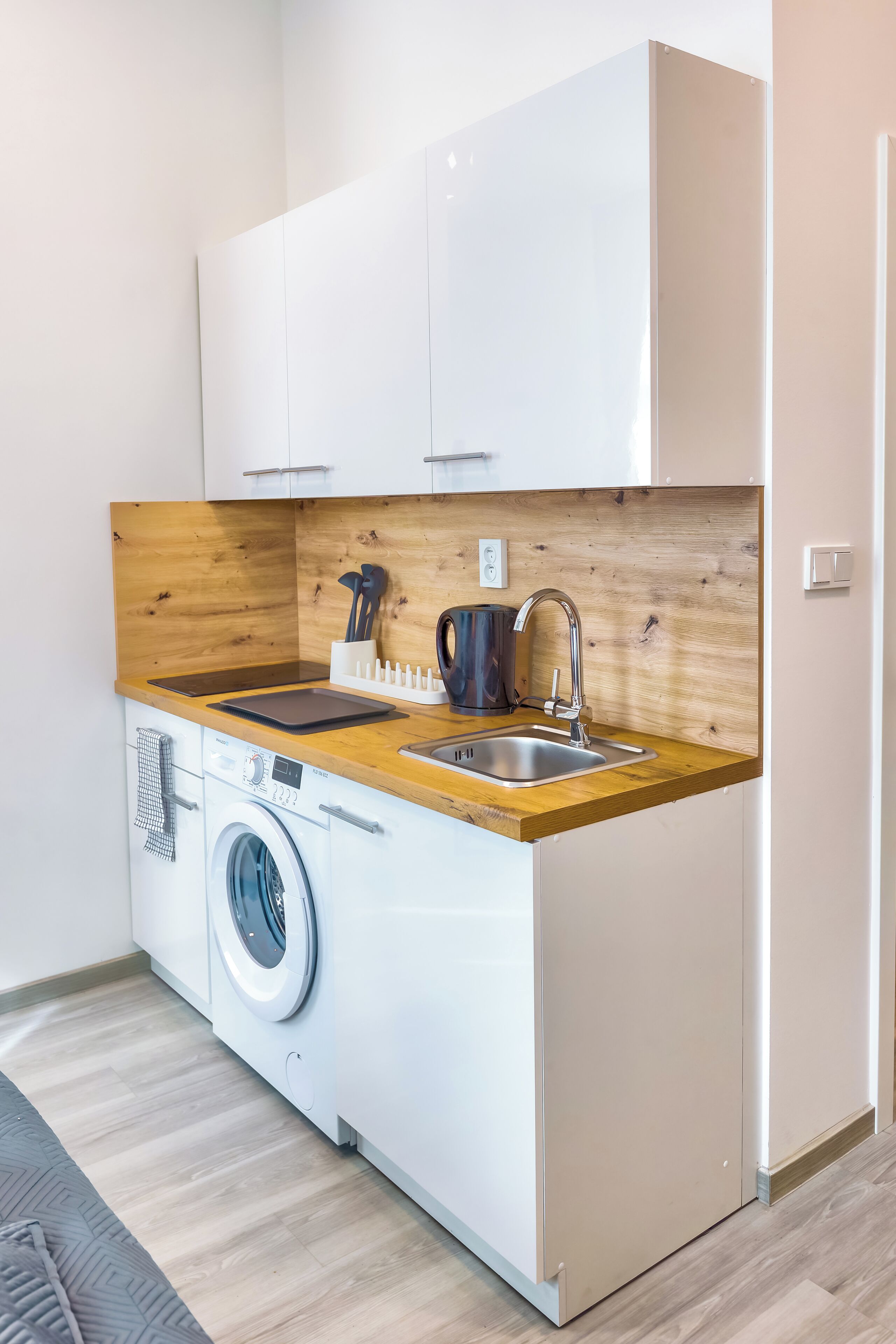 A compact kitchen with a washing machine, wooden countertop, and white cabinets.