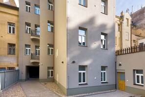 Un edificio residencial de varios pisos con balcones, una entrada porticada y un patio empedrado.