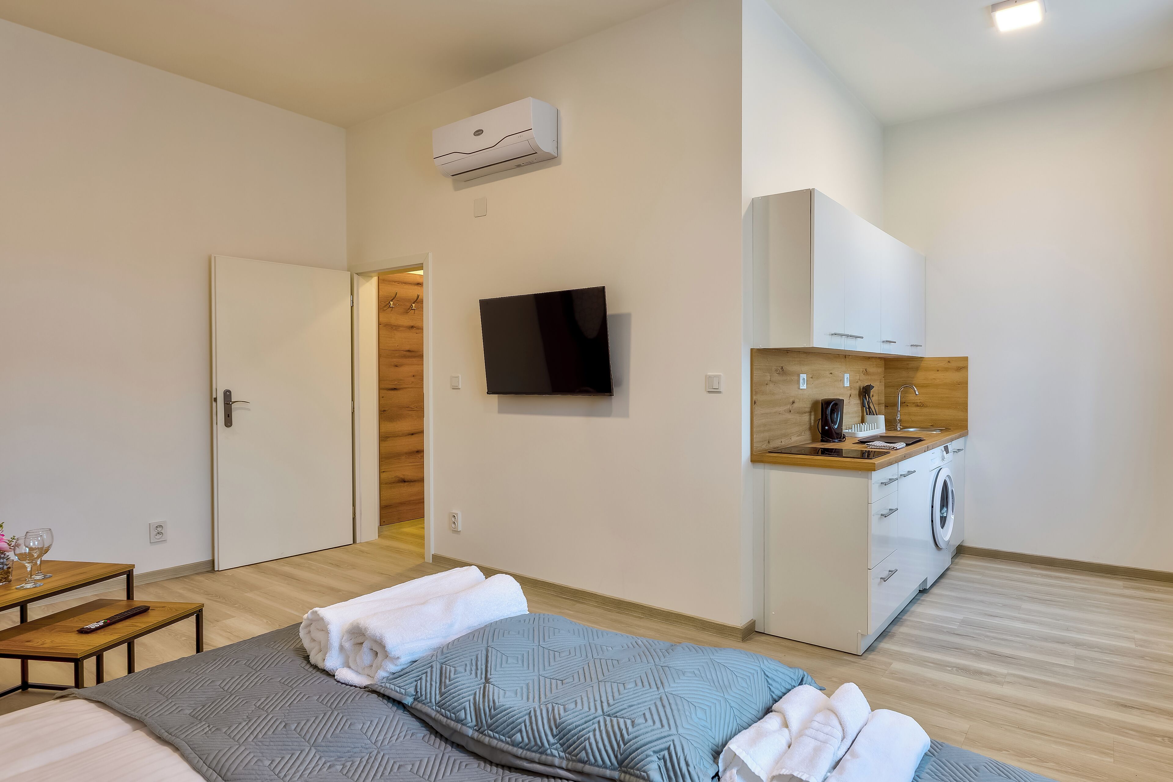 Ett modernt hotellrum med en säng, en TV, en liten köksdel och en väggpanel av trä.