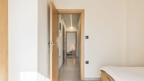 A narrow hallway leading to a bedroom with a wooden bed frame and a white mattress. - Aether by halu (Thessaloniki)