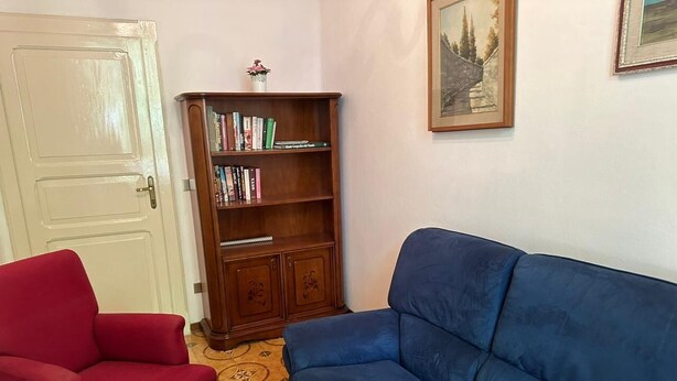 A living room with a red armchair, a blue sofa, a wooden bookshelf, and a framed picture on the wall. - Golden House (Castrocaro terme)