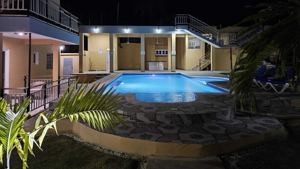 A swimming pool with a tiled deck, a covered area with a bar, and a staircase leading to a balcony. - Luxury 8 King BR  w/ Private Pool, & Event Space (Sosua)