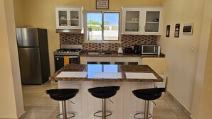 A kitchen with a central island, three bar stools, a refrigerator, a stove, and cabinets. - Luxury 8 King BR  w/ Private Pool, & Event Space (Sosua)