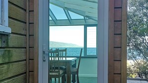 A wooden exterior with a glass door leading to an outdoor seating area with a table and chairs. - Esplanade Azure Horizon (Wellington)