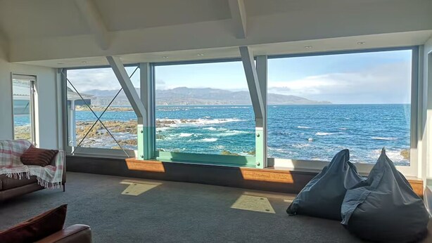 A room with a large window overlooking the ocean, a sofa, and bean bags. - Esplanade Azure Horizon (Wellington)