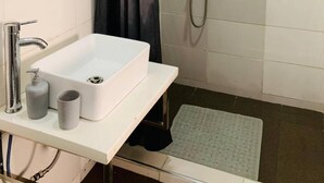 A bathroom with a white sink, a mirror, a shower with a handheld showerhead, and a dark curtain. - 3 Bed Apartment at a Central Location (Ibadan)