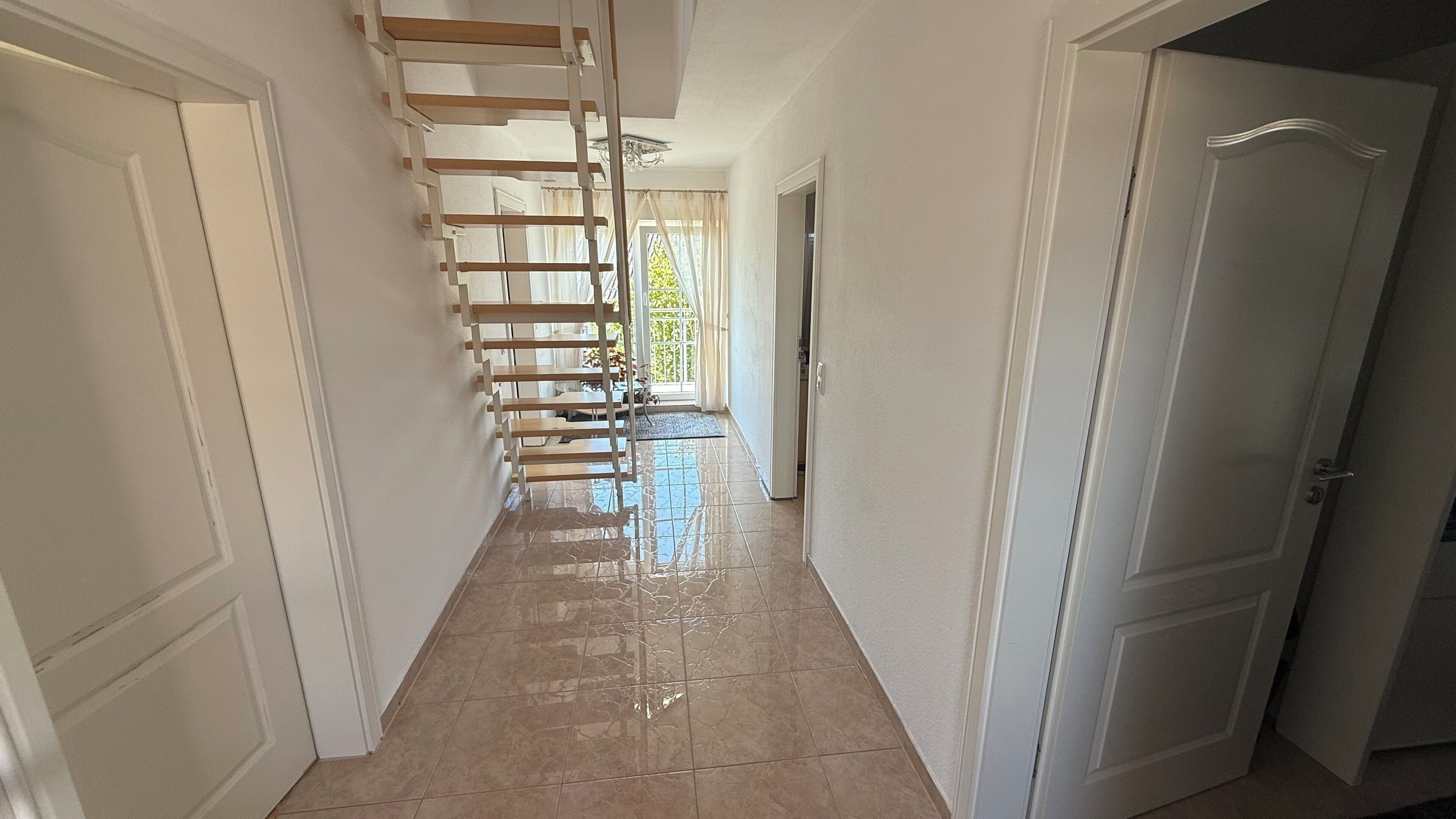 A hallway with a staircase, white walls, and a tiled floor.