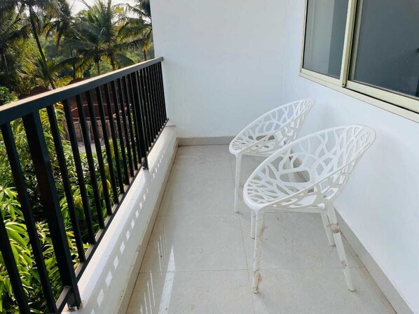 Un balcon avec deux chaises blanches et une rambarde noire.