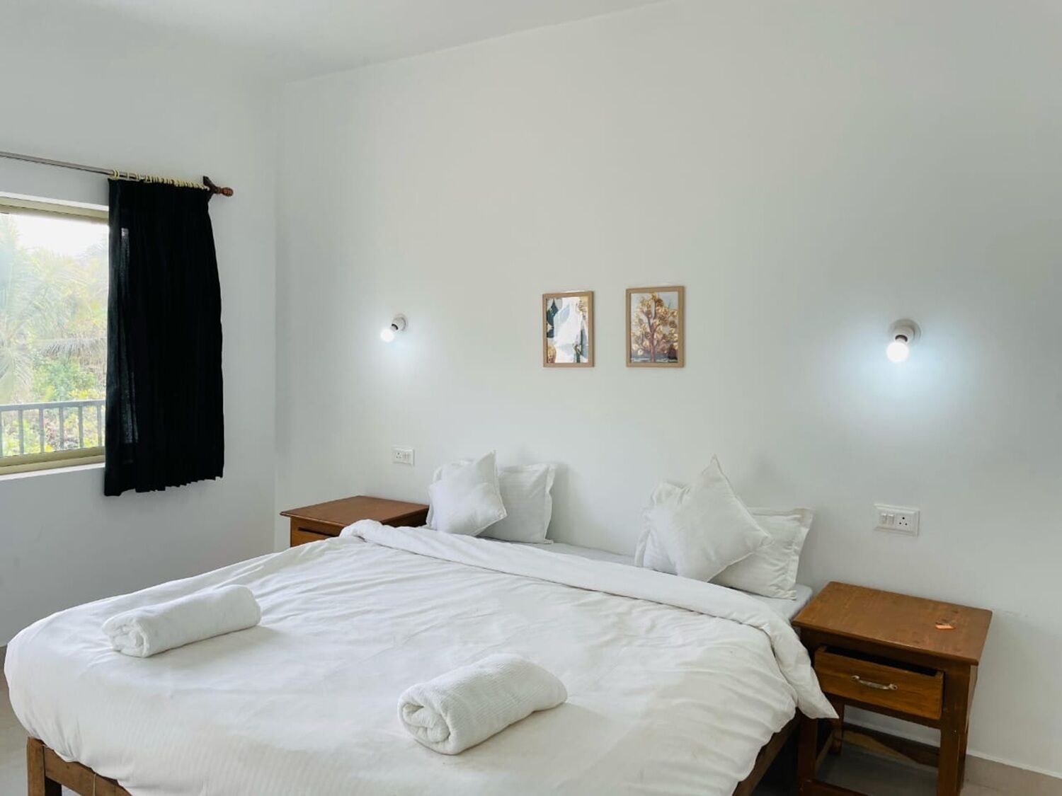 A neatly made bed with white linens and towels, two bedside tables with lamps, and two framed pictures on the wall.