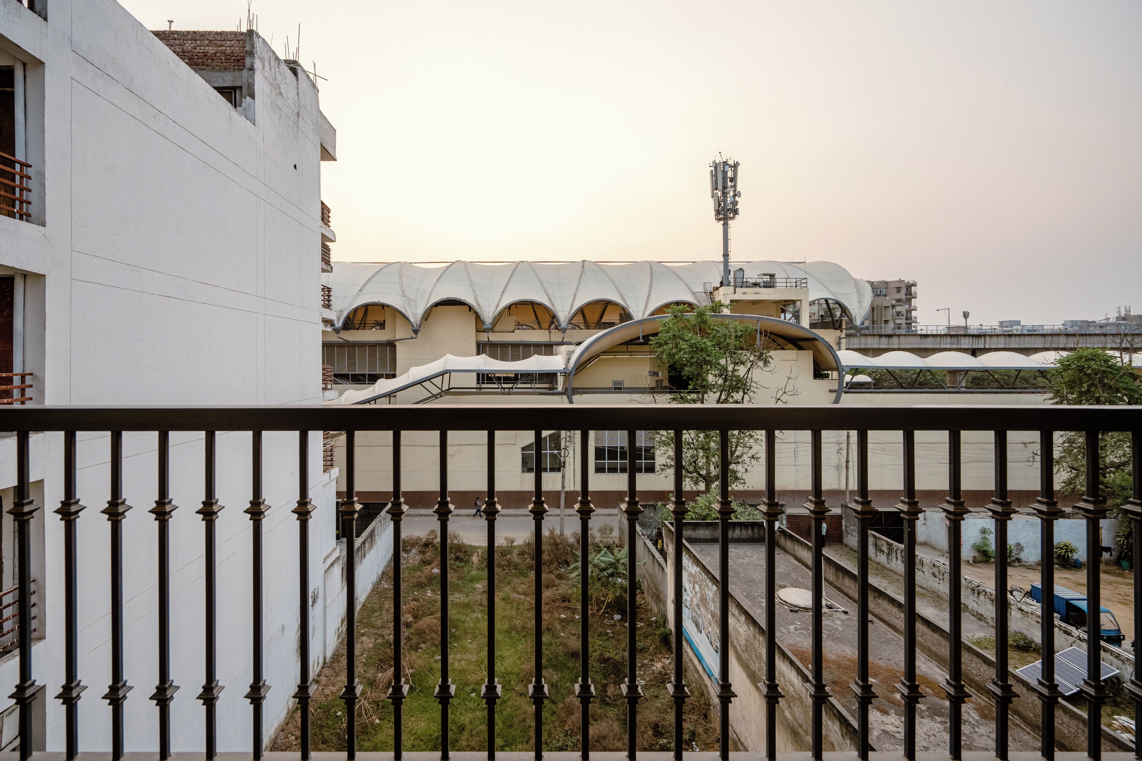 Un bâtiment à la façade blanche, doté d’un balcon avec une rambarde en métal, et dont on aperçoit un pont au loin.