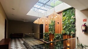 A modern lobby with a checkered floor, a glass railing, hanging pendant lights, a wooden wall with greenery, and a skylight. - Royal Studio Golf Course Road (Sohna)