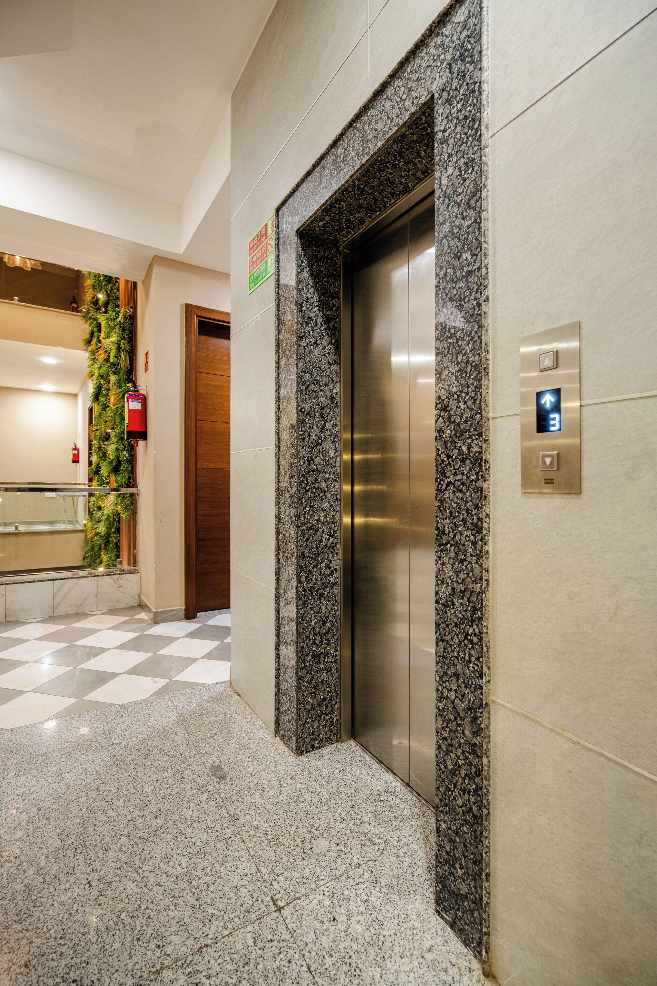 An elevator with a granite border, a fire alarm, and a checkered floor.