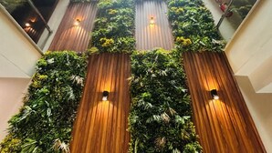 A modern interior with a central wooden staircase flanked by vertical gardens. - Royal Studio Golf Course Road (Sohna)