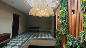 A spacious atrium with a checkered floor, a hanging woven light fixture, and a vertical garden wall. - Royal Studio Golf Course Road (Sohna)