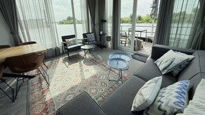 Ett modernt vardagsrum med en soffa, fåtöljer, ett soffbord och ett matbord. Stora fönster ger utsikt över vattnet.