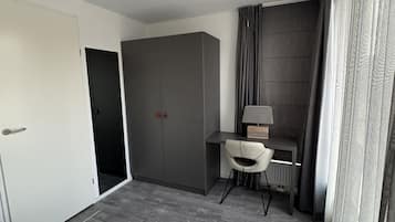 A modern hotel room with a bed, a desk with a chair, a wardrobe, and a bathroom door.