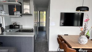 A modern kitchen with a central island, a dining area with a wooden table and leather chairs, and a flat-screen TV mounted on the wall. - Maasterp - Watervillage 14 (Ohé en Laak)