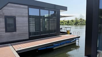 Une maison flottante moderne dotée de grandes fenêtres, d’une terrasse et d’une petite piscine.
