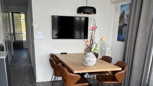A modern dining area with a wooden table, leather chairs, a vase with flowers, a flat-screen TV, and a fan. - Maasterp - Watervillage 14 (Ohé en Laak)