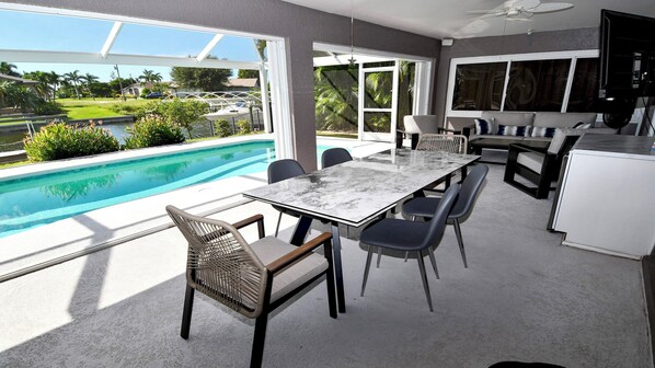 A modern outdoor dining area with a pool view, featuring a marble table and wicker chairs. - Mei Jing Waterfront Pool and Tiki Hut-must see (Cape Coral)