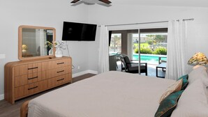 Ein Schlafzimmer mit einem großen Bett, einer Holzkommode, einem Fernseher und Blick auf einen Pool und Sitzgelegenheiten im Freien.