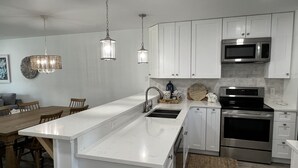 A modern kitchen with white cabinetry, stainless steel appliances, and pendant lighting. - Huge beach-side townhouse located steps to the sand in Mexico Beach! (Mexico Beach)