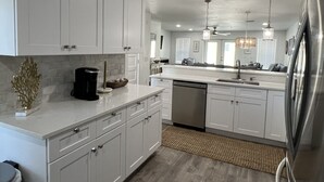 A modern kitchen with white cabinets, a dishwasher, and a stainless steel refrigerator. - Huge beach-side townhouse located steps to the sand in Mexico Beach! (Mexico Beach)
