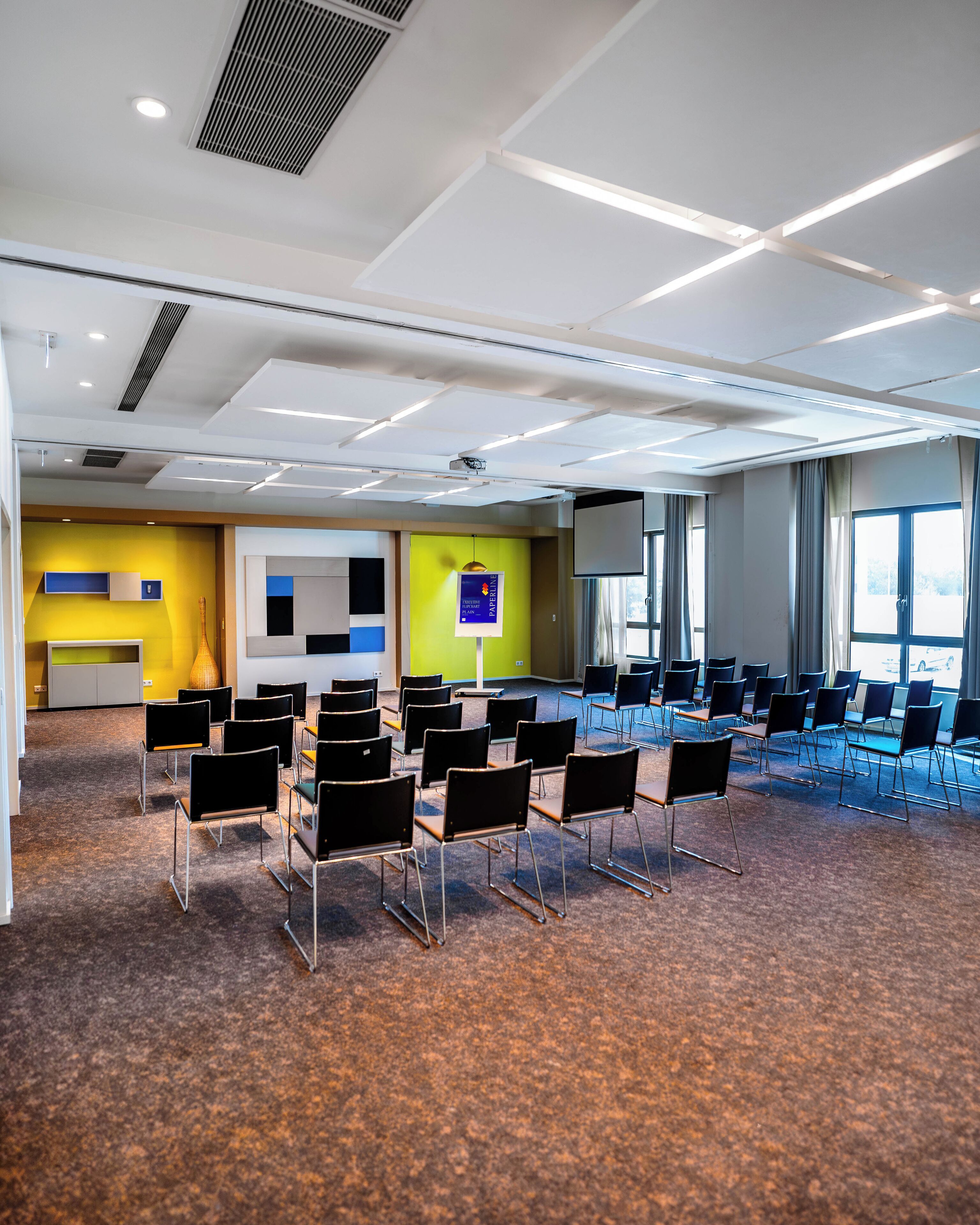 Une salle de conférence avec des rangées de chaises, un écran de projection et un tableau de présentation.