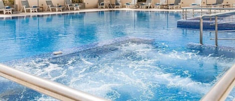 Una piscina al aire libre, sombrillas, sillones reclinables de piscina