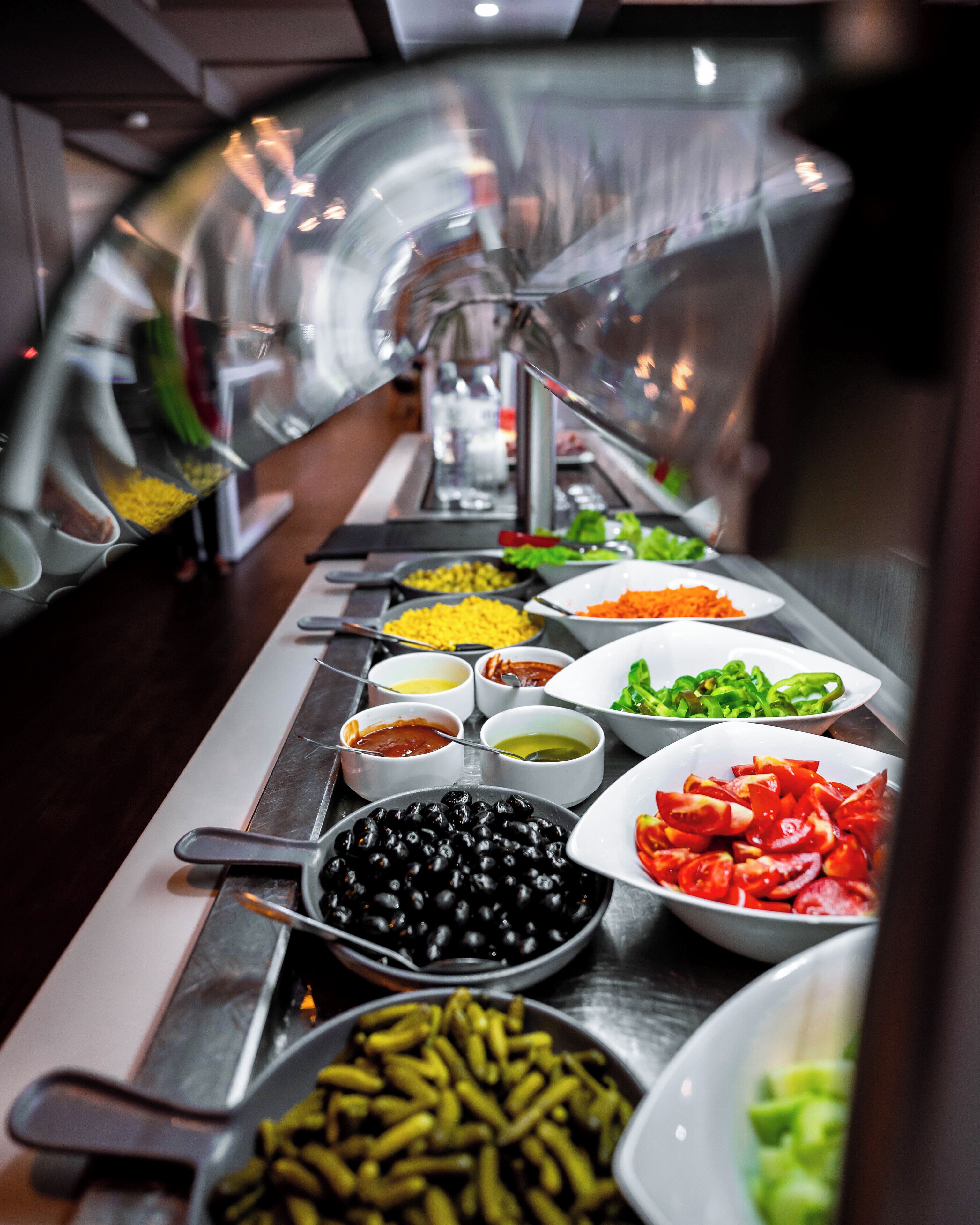 Buffet com diversos alimentos, incluindo azeitonas, tomates e pimentões verdes.