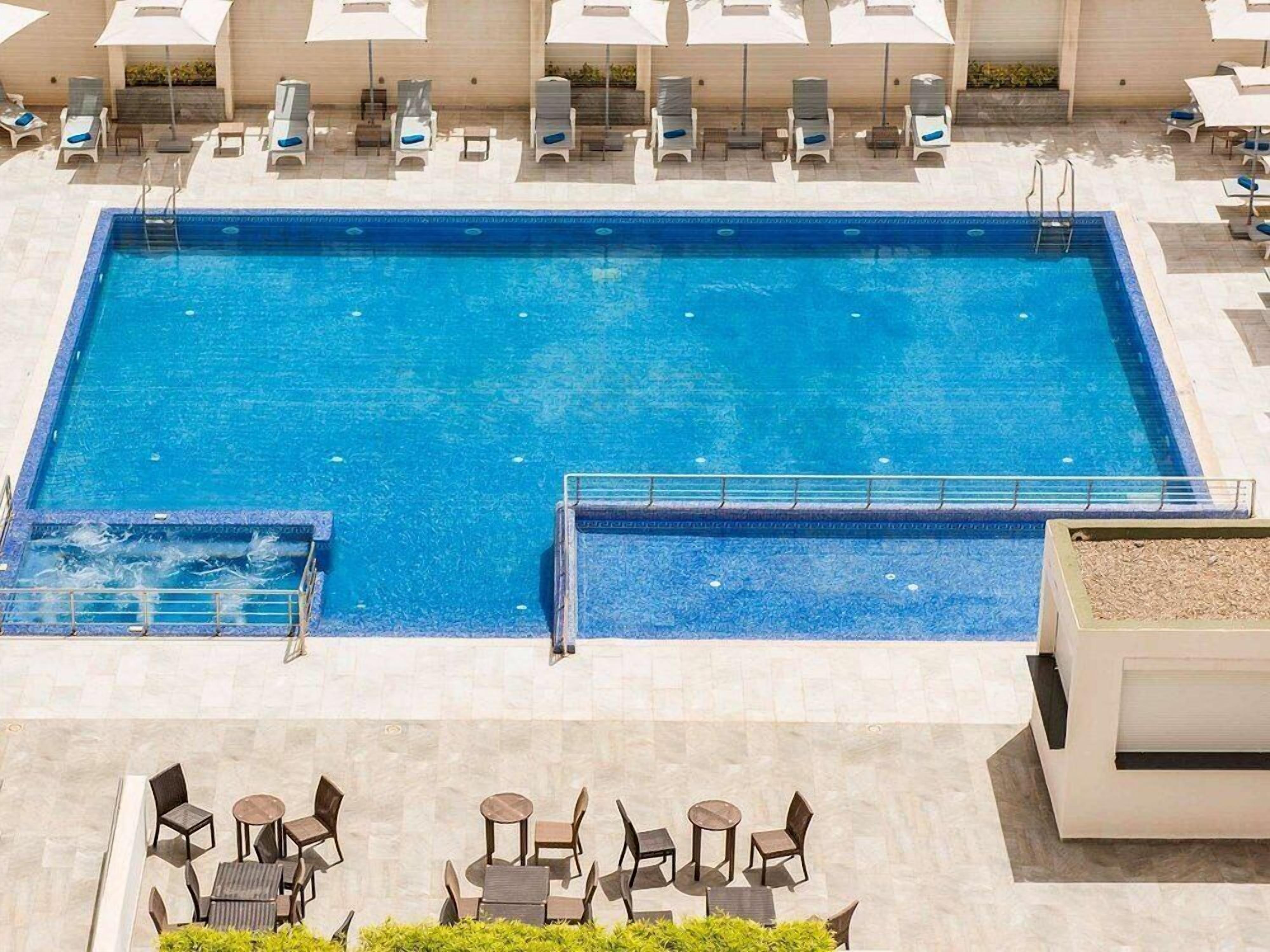 Une piscine rectangulaire à l’eau d’un bleu limpide, entourée de chaises longues et de transats.