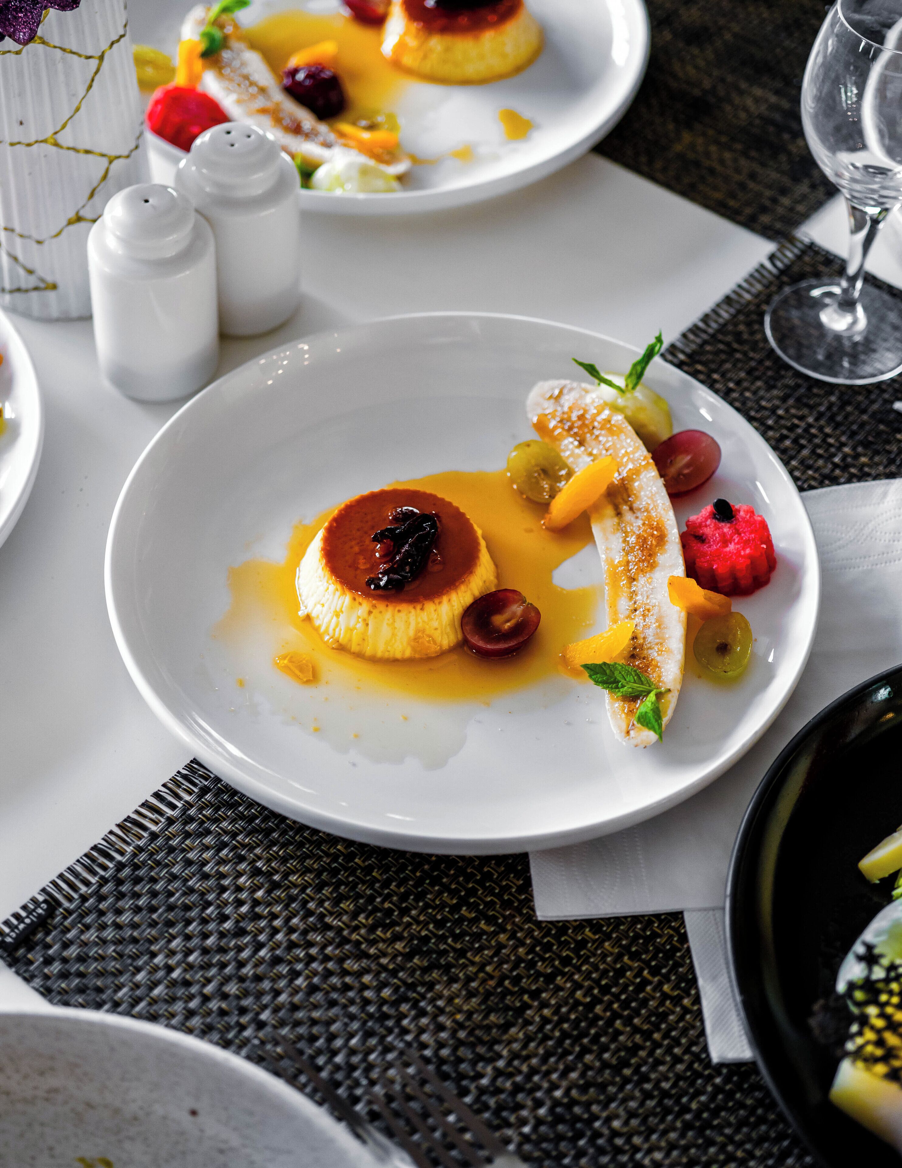 A dining table with a white plate of dessert, a glass of wine, and salt and pepper shakers.