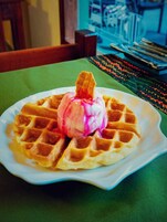 Un plato con un gofre y una porción de helado rosa sobre un mantel verde.