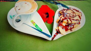 Een stapel pannenkoeken met stroop, een kop koffie, een rode bloem en een pakje Selati.