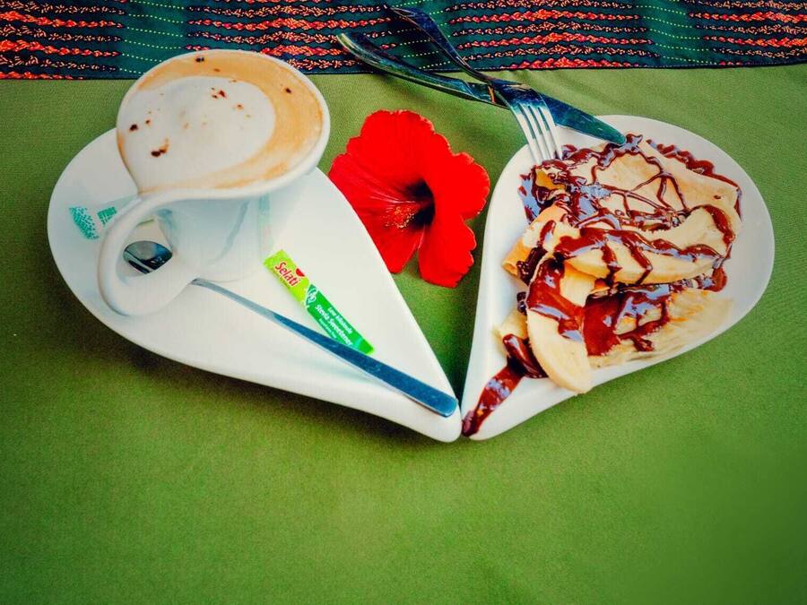 Een stapel pannenkoeken met stroop, een kop koffie, een rode bloem en een pakje Selati.