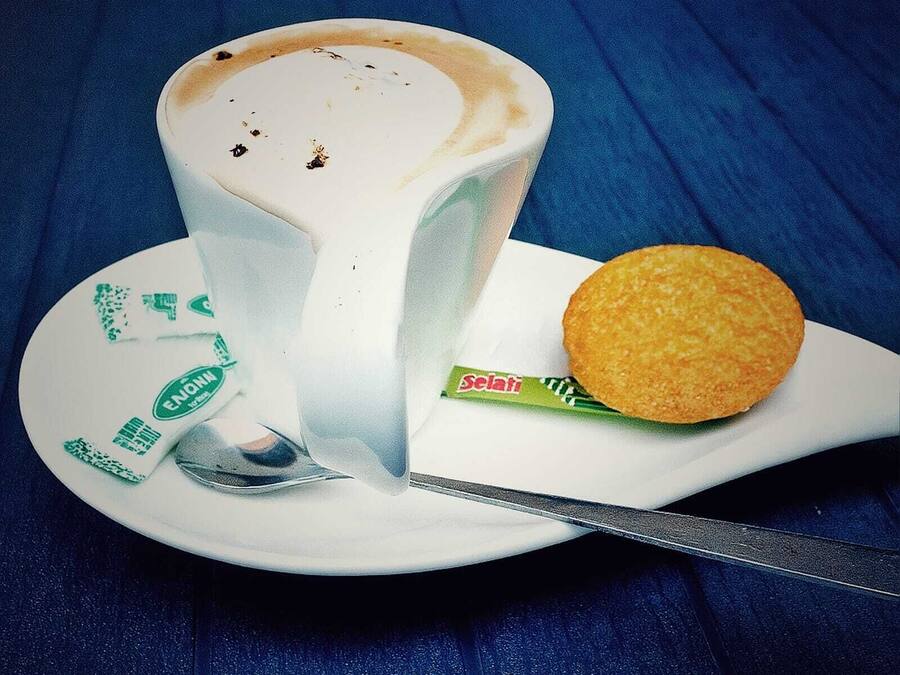 Una taza de café con una cuchara y una galleta sobre un platillo.