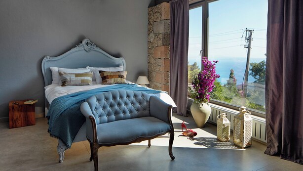 A bedroom with a large bed, stone wall, and a view of the sea. - Mila House (Ayvacik)