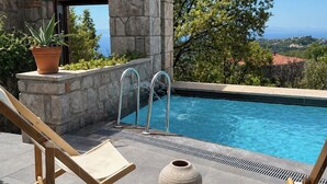 A poolside area with a stone structure, a potted plant, a wooden chair, and a table with a vase. - Mila House (Ayvacik)