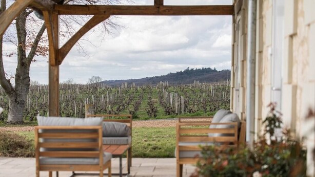 A wooden pergola with two chairs and a table, overlooking a vineyard.