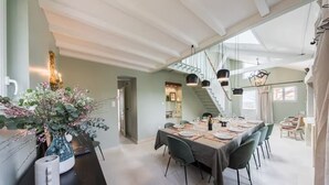 A dining area with a long table set for six, surrounded by chairs, with a staircase leading to an upper level.