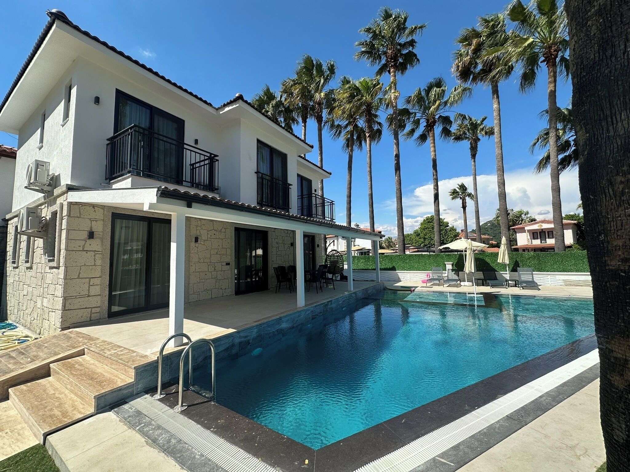 Une maison moderne à deux étages, dotée d’une piscine, d’une façade en pierre et d’un patio couvert.