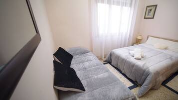 Une chambre d’hôtel avec deux lits, une table de chevet avec une lampe, un tableau encadré au mur et une fenêtre avec des rideaux légers.