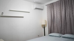 A bedroom with a bed, a bedside table, a lamp, and an air conditioning unit.