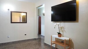 A hallway with a television mounted on the wall, a mirror, and a small table with a potted plant.