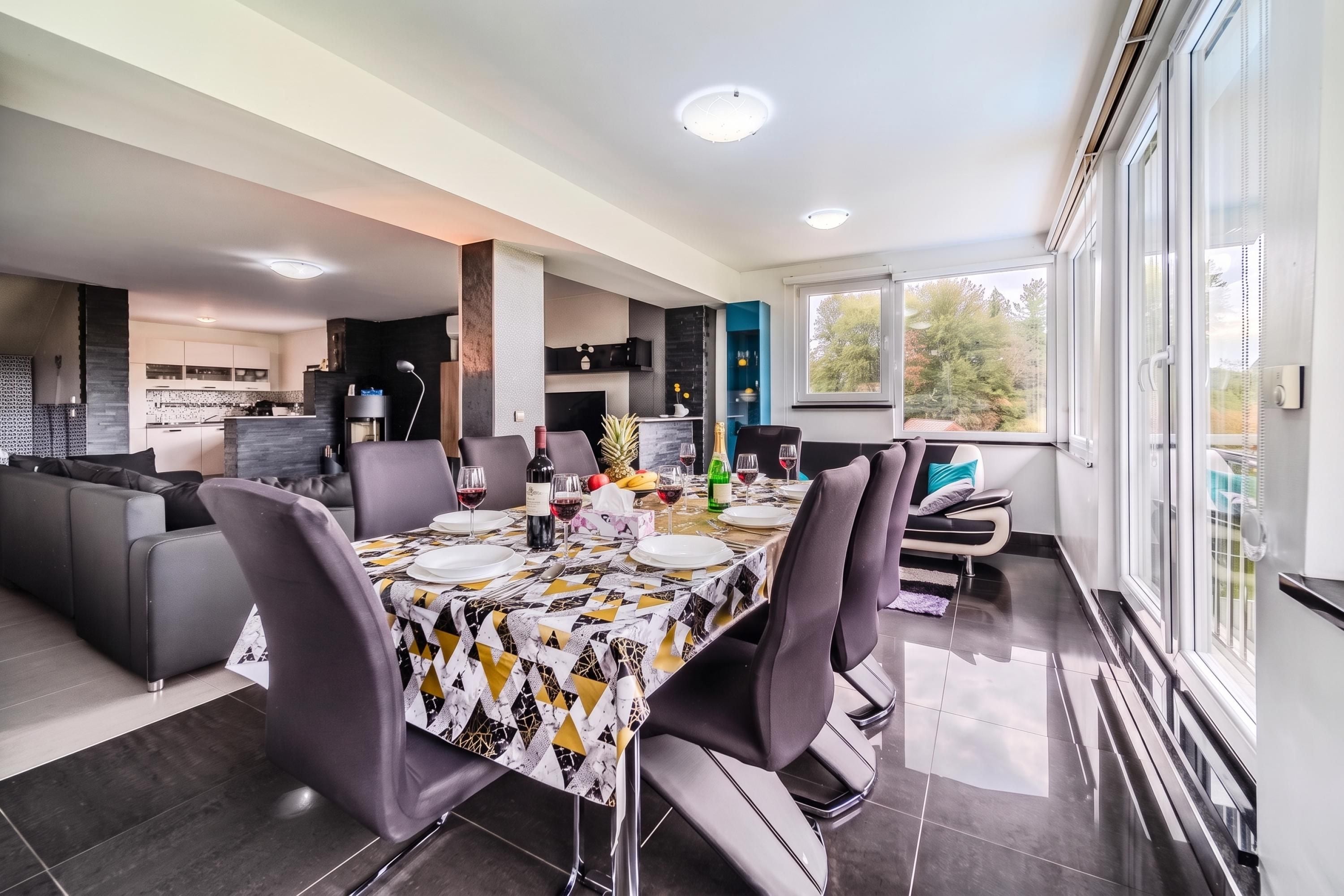 Un comedor moderno con una mesa dispuesta para cuatro personas, rodeada de sillas, en una habitación luminosa con un amplio ventanal.