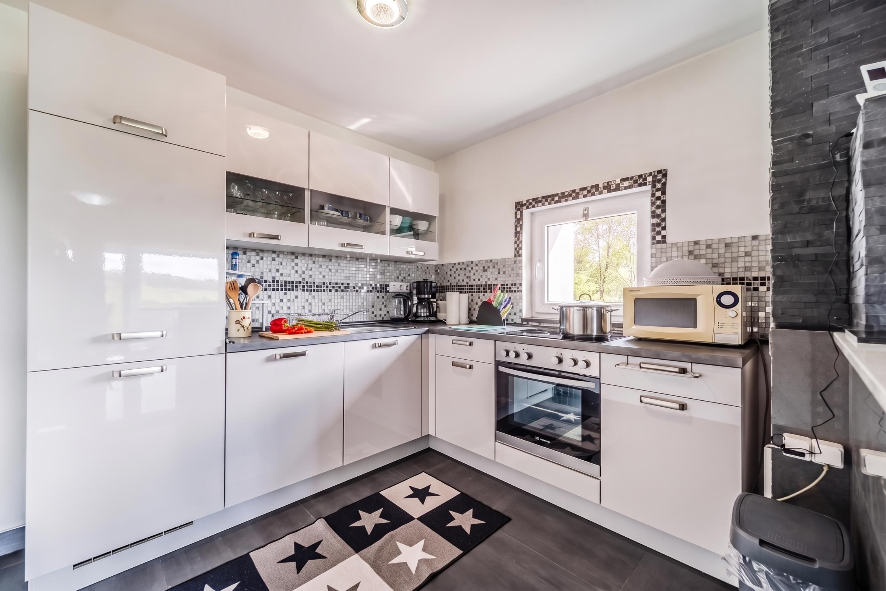 Une cuisine moderne avec des meubles blancs, un four à micro-ondes, une cuisinière et un évier.