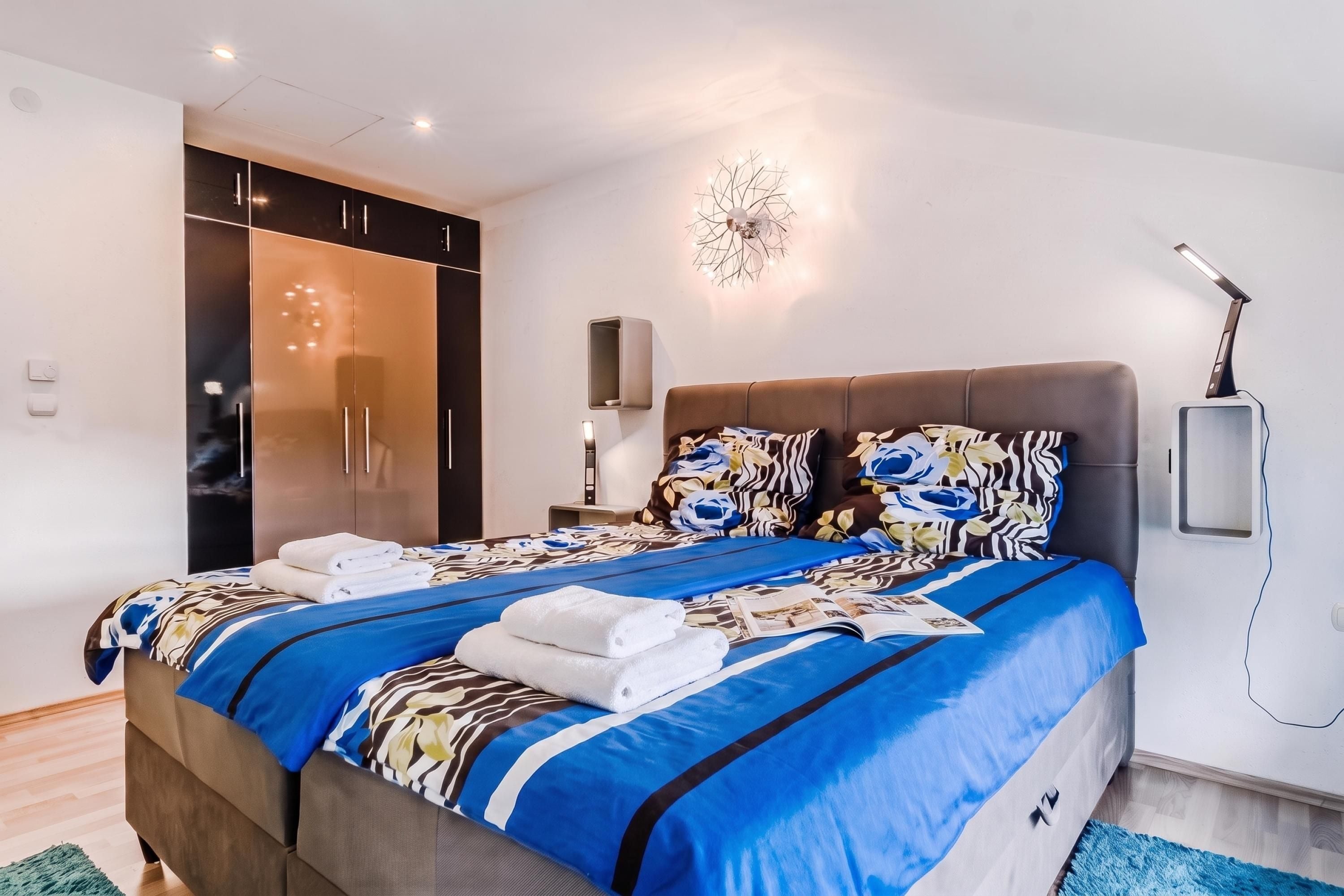 Een moderne slaapkamer met een groot bed, een kledingkast, een nachtkastje en een wandlamp.