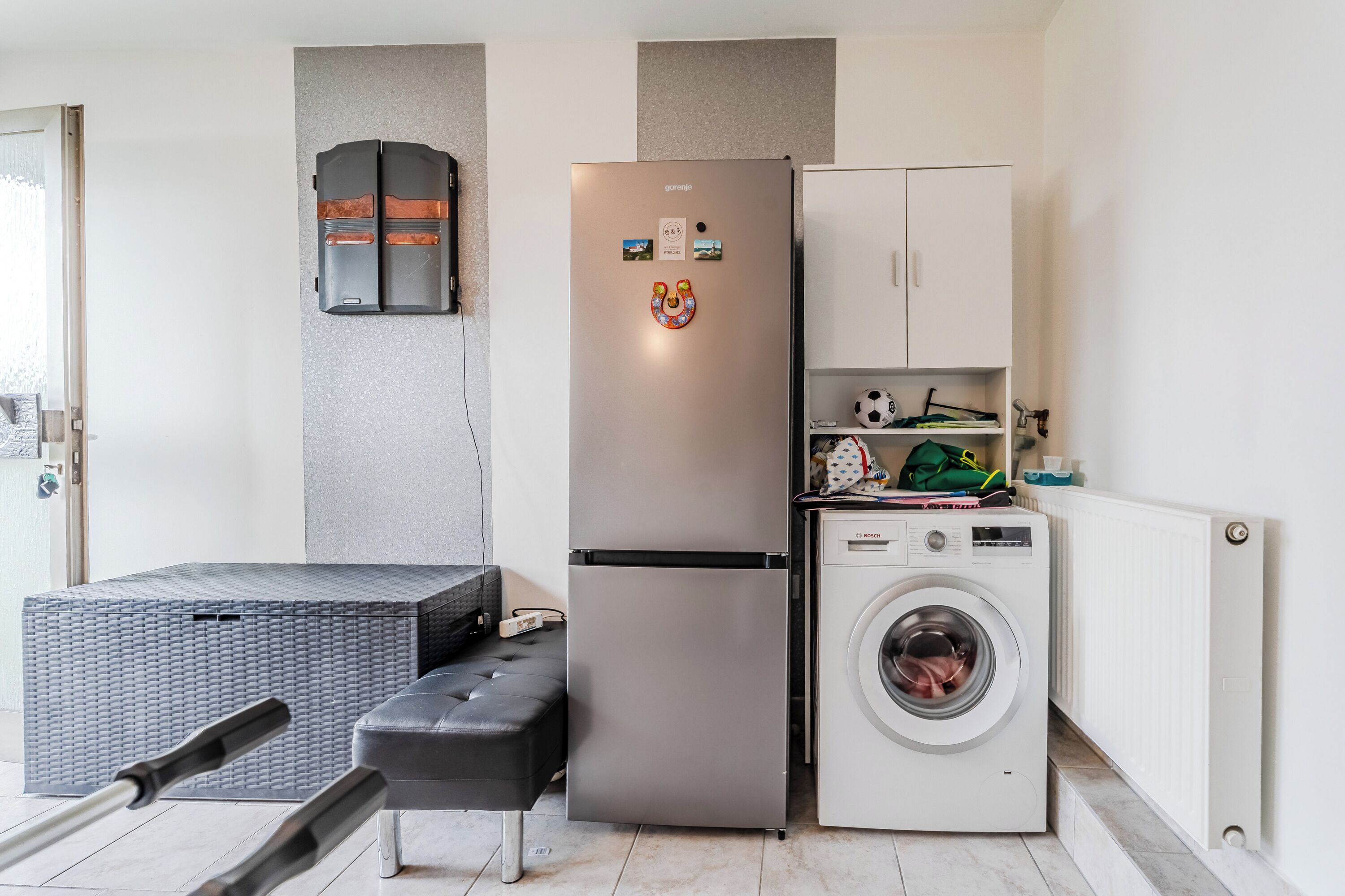 A compact kitchen with a stainless steel refrigerator, a washing machine, and a small cabinet.