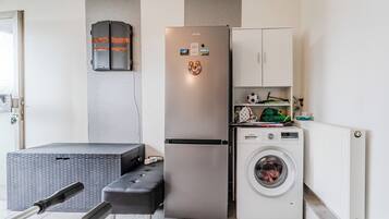 A compact kitchen with a stainless steel refrigerator, a washing machine, and a small cabinet.