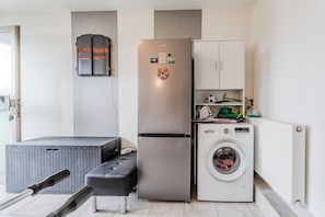 A compact kitchen with a stainless steel refrigerator, a washing machine, and a small cabinet. - Riverside House With Pool and Hot Tub (Karlovac)